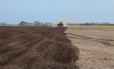 Tractor cultivating field in spring, harrowing of land, selective focus on land with fertilizer,...