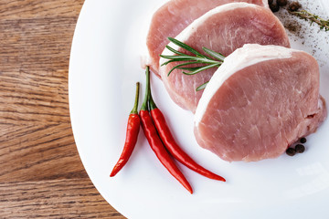 Fresh pork meat with garlic, hot pepper on a branch and rosemary. On a white plate. Above view.