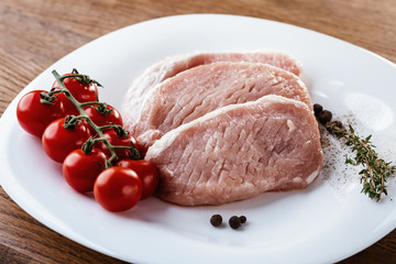 Fresh pork meat with garlic, tomatoes on a branch and rosemary. On a white plate. Above view.