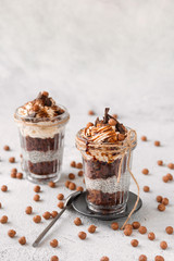 Layered small dessert with chocolate sponge cake, yogurt with Chia seeds and whipped cream in serving glasses on a light background
