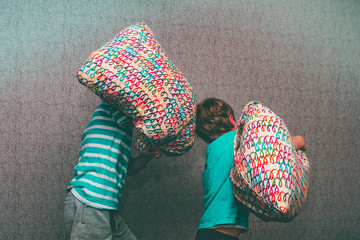 Two brothers of a European boy fight with pillows on the bed. A merry duel of children.