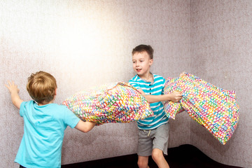 Two brothers of a European boy fight with pillows on the bed. A merry duel of children.