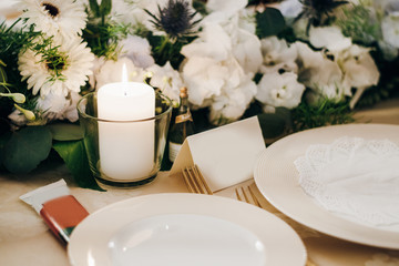 Festive table decorated with fresh flowers, candles, plates, forks and empty cards