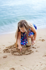 A little girl plays in the sand near the water