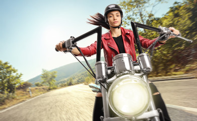 Fototapeta na wymiar Young female biker riding a custom motorbike on road