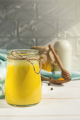 Glass jar with a healthy drink of golden milk made from turmeric, milk and pepper on a white wooden background. Prevention of diseases and viruses.