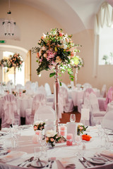 Beautiful wedding round table for guests, decorated with flower composition, candles, tableware,...