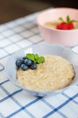 Healthy homemade oatmeal porridge with berries for breakfast in ceramic bowl on a checkered tablecloth.