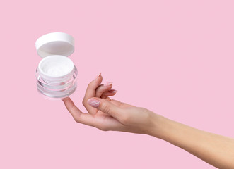 Open jar with cosmetic cream with womans hand on pink background.