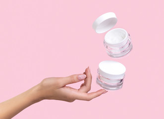 Open jar with cosmetic cream with womans hand on pink background.