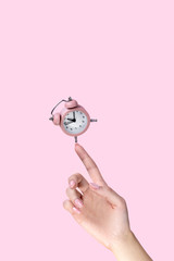 Alarm clock balancing on womans hand on pink background