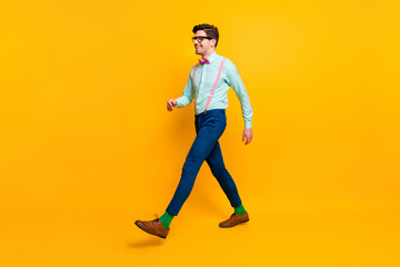 Fototapeta na wymiar Full length profile photo of cool stylish guy boyfriend walking down street date girlfriend wear specs shirt bow tie suspenders trousers shoes isolated vivid yellow color background