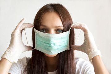 Young woman wearing rubber gloves putting on a face mask as virus protection.
