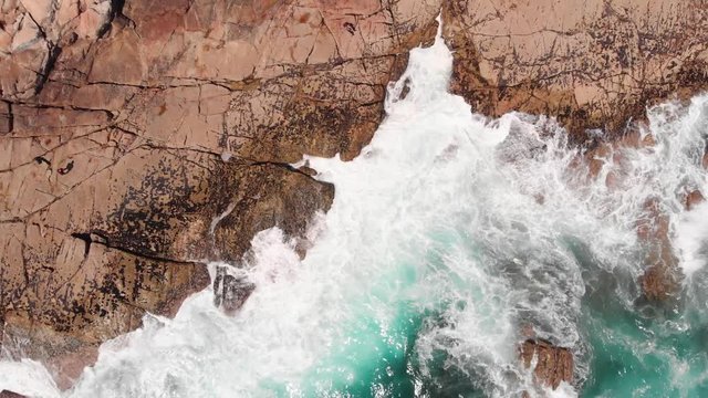 Drone rocket view of waves crashing intro rocky shore during daytime
