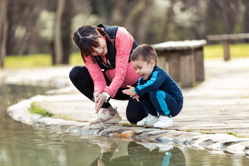 Pretty young mother with her little son playing with the water in the pond.