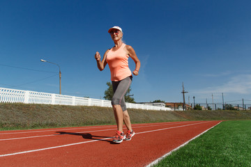 an elderly fit woman in a t shirt and breeches runs at a sports stadium