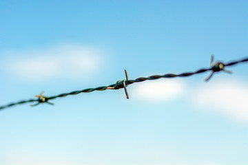 Close up barbed wire fence against blue sky.