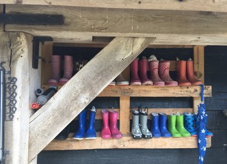 Colourful children boots on wooden shelf at petting zoo, with children umbrella and thermometer