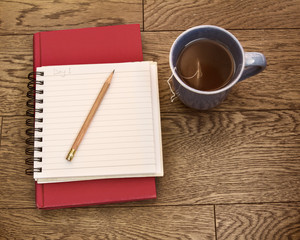 Notebook open with sharp pencil, book and cup of tea; Journal open for reflection with some warm tea