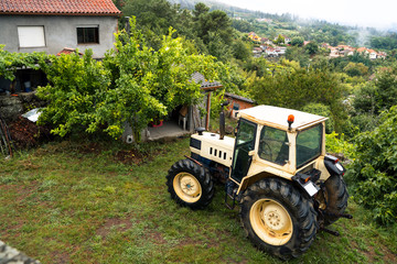 Horizontal top view of countryside tractor in the north of Spain, Galicia. Winter seasonal time. Humidity and rainy weather inside home. Nature rural landscape on green field with rustic houses.