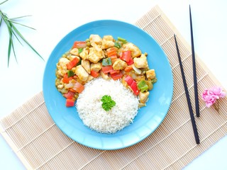 Asian chop suey with vegetables and chicken breasts served on a blue plate with rice decorated with curly parsley closeup on a white background with chopsticks and cherry blossoms with blank space.