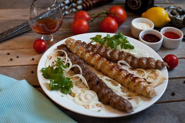 Lula kebab meat dish on a plate with greens tomatoes and sauce on a wooden background