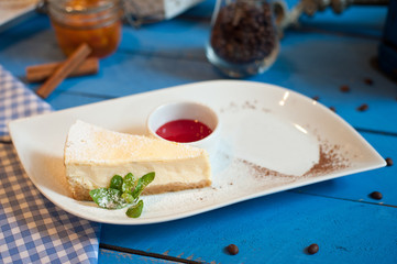 cheesecake on a white plate with a sprig of mint on a blue wooden background raspberry sauce on a white plate