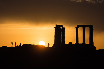 Obraz premium People visiting and taking photos of the famous ancient temple of Poseidon in Cape Sounio near Athens Greece during sunset with the sun setting over the horizon