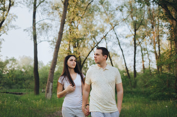 Fototapeta premium Loving, beautiful, stylish guy and girl in tracksuits strolling through the forest, holding hands, outdoors in the park. Love story newlyweds. Photography, concept.