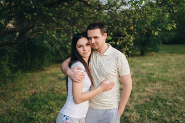 Lovers, beautiful, stylish guy and a girl in tracksuits hug in the forest, outdoors in a green garden. Love story newlyweds. Photography, concept.