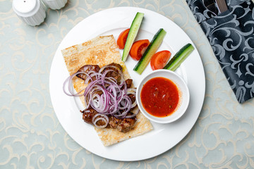Kebab of veal on a white plate with tomato sause