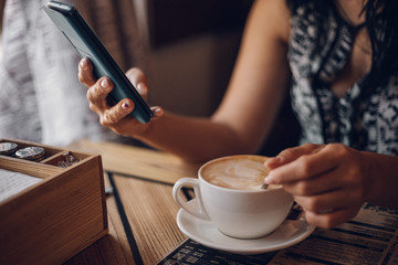 Girl in a cafe drinks cappuccino and holds a smartphone in her hands