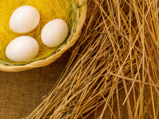 Three eggs in a basket on burlap next to the straw. The concept of celebrating the Christian holiday of Easter. Organic farm products.