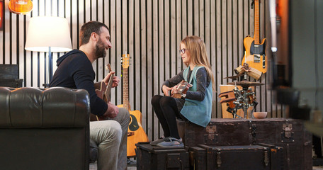 Dad teaching guitar and ukulele to his daughter.Little girl learning guitar at home.Side view.Ukulele class at home. Child learning guitar from her father