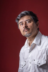 Retrato de hombre latino con camisa blanca sobre fondo rojo oscuro