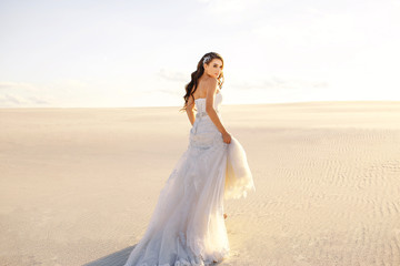 beautiful bride in a beautiful long dress walks on the sand in the desert, backlight, sunset,...