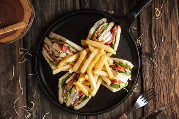 Top view on sandwiches with fries on the black pan on the wooden table, horizontal format