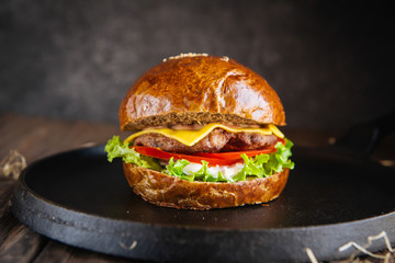 Side view closeup of a burger with a rye dark bun on the black pan on the wooden table dark background, horizontal