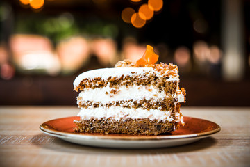 Side view closeup on a piece of 
cheese cream carrot cake on the wooden table with blurry bokeh...