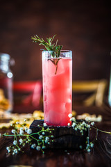 Side view on sweet pink fruit cocktail in glass on the wooden board on the wooden table with decorative elements, vertical format