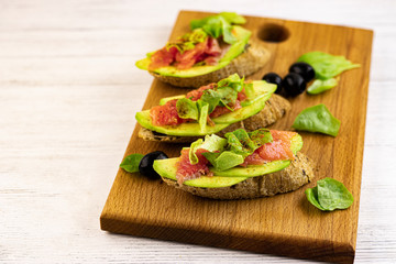sandwiches of fresh avocado and red fish on a wooden tray, top view