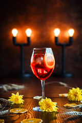 Side view of delicious sweet aperol alcohol cocktail in wine glass on the wooden table with yellow flowers as decorative elements, vertical