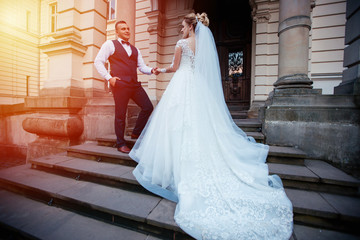 Obraz premium The bride and groom walk together in the park. Charming bride in a white dress, the groom is dressed in a dark elegant suit.