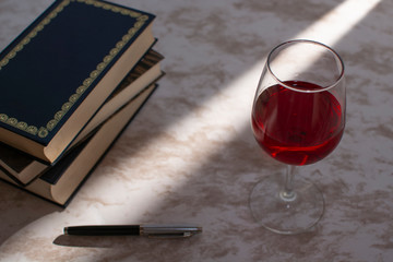 Copa de vino acompañada de unos libros con la luz de la venta entrando por un costado