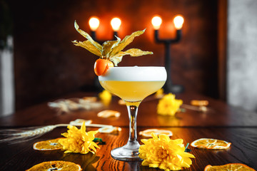 Side view on the delicious sour alcohol cocktail in a glass on the wooden table with yellow flowers...