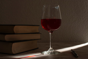 Copa de vino acompañada de unos libros con la luz de la venta entrando por un costado