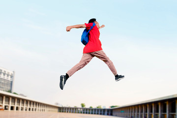University student jumping in the air with his bag