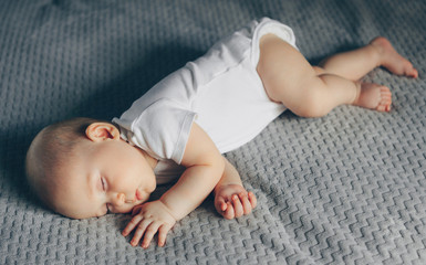 Sleeping baby boy in white bodysuit in bed
