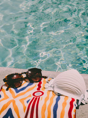 Face mask, a towel and a pair of sunglasses laying beside a swimming pool