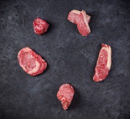 Variety of Raw Black Angus Prime meat steaks on a dark background